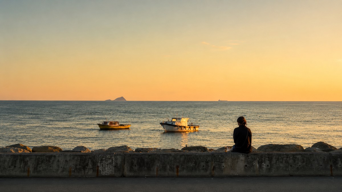 A person sitting alone at dusk, watching two boats on a calm harbor
